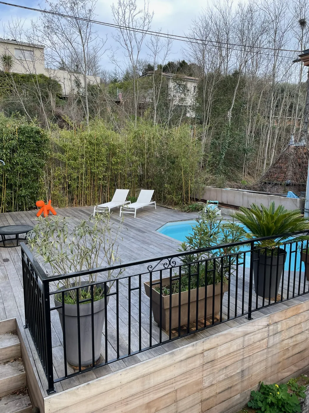 Garde-corps en fer forgé noir à volutes ceinturant une terrasse en bois au bord d'une piscine, fabrication sur mesure ManufactureVB